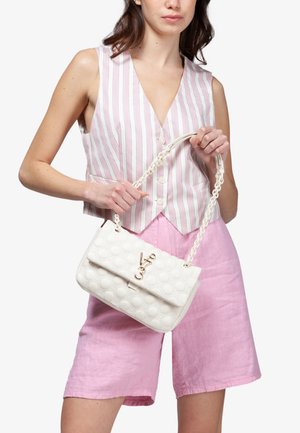 Donna con gilet senza maniche a righe rosa e bianche e pantaloncini rosa che tiene una borsa trapuntata bianca con tracolla a catena dorata e chiusura con logo.