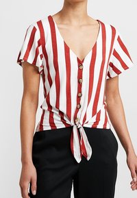 Červený a bílý pruhovaný kr�átký rukáv top s hlubokým výstřihem do V a zavazováním vpředu, s knoflíkovými detaily uprostřed. Hladký povrch látky.