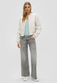 Weißer, gekürzter Sweatshirt mit Rundhalsausschnitt und Druckknöpfen, kombiniert mit verwaschenen grauen, weiten Jeans und weißen Sneakers.