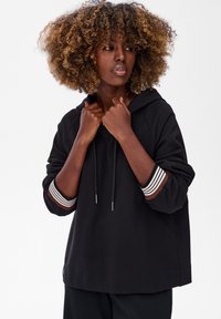 Czarna bluza z kapturem z kieszenią z przodu, sznurkiem i paskami na mankietach w kolorze brązowym, białym i czarnym. Miękki materiał, luźny krój.