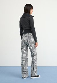 Black textured jacket with a wide collar paired with patterned black-and-white flared pants featuring floral designs and black sneakers.