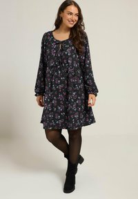 Mustakukkainen mekko pitkillä hihoilla, jossa on solmittava kaula-aukko, strukturoidusta kankaasta ja rento malli. Yhdistetty mustiin nilkkasukkiin.