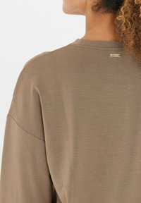 Brauner Baumwollpullover mit einer lockeren Passform, rundem Ausschnitt und einem kleinen Metall-Logo auf der Rückseite. Glatte Textur mit minimalistischer Gestaltung.