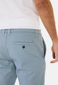 Lichtblauwe, katoenen broek in een mixmateriaal met een gestructureerde afwerking, voorzien van een achterzak met knoopsluiting en zijzakken.