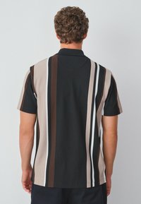 Kortärmad polo skjorta med vertikala ränder i svart, brunt, beige och vitt. Ribbad textur med en klassisk krage.