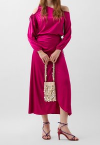 Ensemble top à épaules dénudées et longue jupe fuchsia, avec poignets élastiqués. Accessoirisé d'un sac à main crème orné de perles et de stilettos multicolores.
