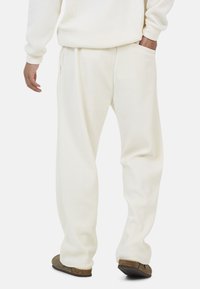 Kremowe, prążkowane spodnie do wypoczynku z bocznymi kieszeniami, luźny krój i teksturowany materiał. Noszone z brązowymi butami wsuwanymi, prezentujące swobodny kształt sylwetki.