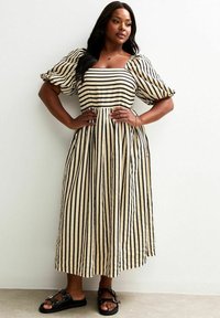Gestreiftes Midikleid in Beige und Schwarz, mit Puffärmeln, einem quadratischen Ausschnitt und einem voluminösen Rock, kombiniert mit schwarzen Sandalen.