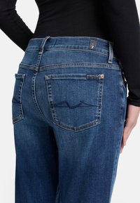 Jeans in denim di colore blu scuro con un taglio dritto. Presentano due tasche posteriori con dettagli di cucitura sottili e un'etichetta con il marchio vicino alla vita.