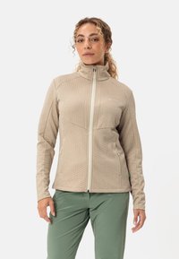 Giacca in fleece beige con un motivo testurizzato a nido d'ape, colletto alto, chiusura frontale con zip e tasche laterali. Dettagli accentati in verde visibili.