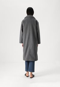 Cappotto grigio in misto lana con ampio colletto, spalle cadenti, dettaglio sulla cucitura posteriore, abbinato a jeans blu tagliati e sandali neri piatti.
