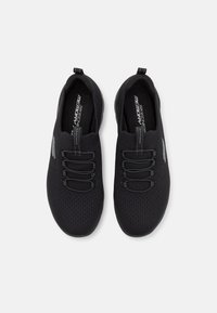 Zapatos negros tipo slip-on con parte superior de malla transpirable, cordones elásticos y plantilla de espuma con memoria. Cuenta con una punta redondeada y un diseño texturizado.