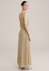 Kuldne maxi kleit, millel on vertikaalsed volangid, õhukesed rihmad ja avatud selg. Omab vormitud vööd ja voolavat seelikut. Elegantne, sädelev tekstuur.