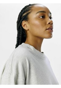 Grå, oversized sweatshirt med en blød tekstur; rund halsudskæring; modellen har fletninger og en neutral baggrund.
