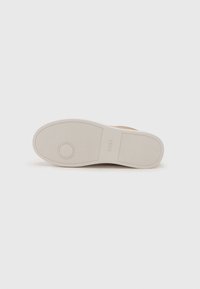 Chaussure en cuir marron avec une semelle en caoutchouc blanche, présentant une surface texturée et un accent circulaire sur la semelle.