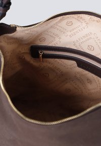 Intérieur d'un sac fourre-tout en tissu marron, comportant une poche zippée et un doublure marron clair avec un motif répétitif du logo "Café Noir". Bordure de fermeture éclair dorée.