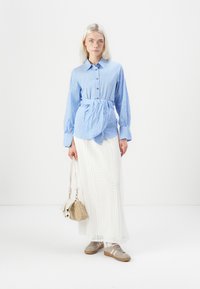 Lyseblå rutete skjorte med knapper og slipsdetalj, kombinert med en hvit blonde maxiskjørt og beige sneakers. Tilbehør: liten håndveske.