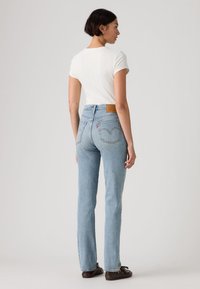 Ανοιχτά μπλε τζιν τζιν με ίσια γραμμή, με πίσω τσέπες και ταμπελάκι από δέρμα ταμπά στη μέση. Συνοδεύονται από άσπρο τοπ.