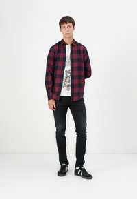 Piros és sötétkék kockás ing, fehér grafikai póló alul, fekete skinny farmernadrág, és fekete sportcipő fehér csíkokkal.