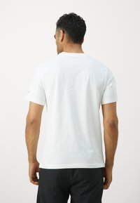 Hvid t-shirt med korte ærmer lavet af bomuld, der har en klassisk rund hals, med et lille rødt detaljer på venstre ærme.