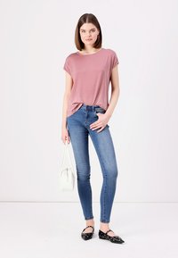 Lichtroze shirt met korte mouwen, slim-fit blauwe jeans, zwarte ballerina's met uitsnijdingen, en een witte handtas. Eenvoudige, casual outfit.
