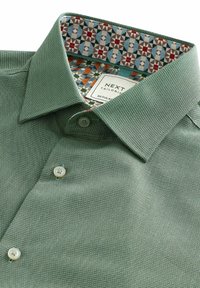 Grünes, strukturiertes Hemd mit einem Button-Down-Kragen. Das Innenfutter zeigt ein mehrfarbiges Muster in Rot, Blau und Grün. Etikett sichtbar.