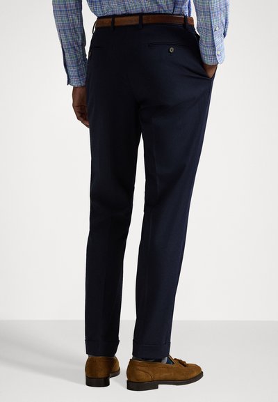 Pantaloni da dress navy con vestibilità su misura, dotati di due tasche posteriori e una texture liscia, abbinati a scarpe in suede marroni.