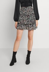 Minifalda negra con flores y volantes, con un delicado estampado sobre una tela transparente. Combinada con botas negras de tobillo ajustadas.
