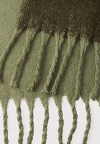 Καφτάνε ριγωτό μάλλινο κασκόλ σε ελιά πράσινο, με υφή στο φινίρισμα, ακανόνιστα τελειώματα με φούντες και διακριτό μοτίβο στην κορυφή. Απαλή και ζεστή εμφάνιση.