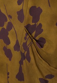 Brauner Stoff mit einer glatten Textur, der mit einem lila Blumenmuster verziert ist. Das Design umfasst sich überlappende Blütenblätter und eine eingekräuselte Nahtdetail.