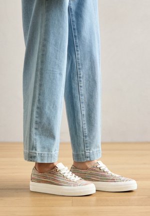 Multicolored woven sneakers with a textured finish, featuring a white rubber sole and white laces, paired with light blue denim pants.