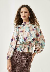Blusa de estampado floral con cuello alto, mangas abullonadas y cintura fruncida. Los colores incluyen verde menta, durazno y púrpura sobre una tela suave.