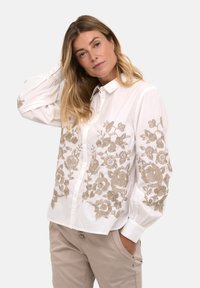 Cămașă albă cu nasturi, având broderie floral�ă complicată în nuanțe de bej pe față și mâneci; realizată dintr-un material ușor, cu o textură netedă.