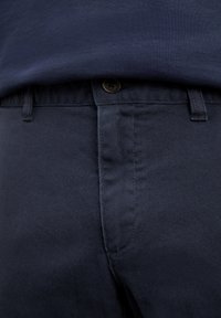 Primer plano de pantalones oscuros azul marino con cintura abotonada y trabillas para cinturón, combinados con una camisa azul marino metida por dentro.