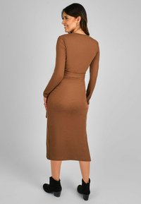 Knee-length, suknelė su raukiniais, ruda, ilgomis rankovėmis, prigludusia liemeniu ir šonu plyšiu, derinama su juodais aulinukais iki kulkšnies.