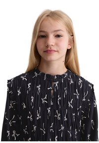 Marineblouse met witte strikpatroon, gerimpelde schouders, geknopte hals en gathered textuur, met een ontspannen pasvorm en zacht materiaal.