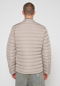 Lichtbeige donzen jas met horizontale stiknaden, opstaande kraag en elastische manchetten, met een logo op de onderrug.