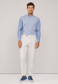 Gestreiftes blau-weißes Button-Up-Hemd, weiße Hose und blaue Turnschuhe. Das Hemd hat einen Kragen und Manschetten; die Hose hat eine Knopfdetails.
