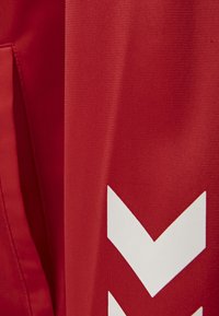 Rødt stof med en struktureret finish har et fremtrædende hvidt chevronmønster. Designet understreger lodrette linjer og klare farver.