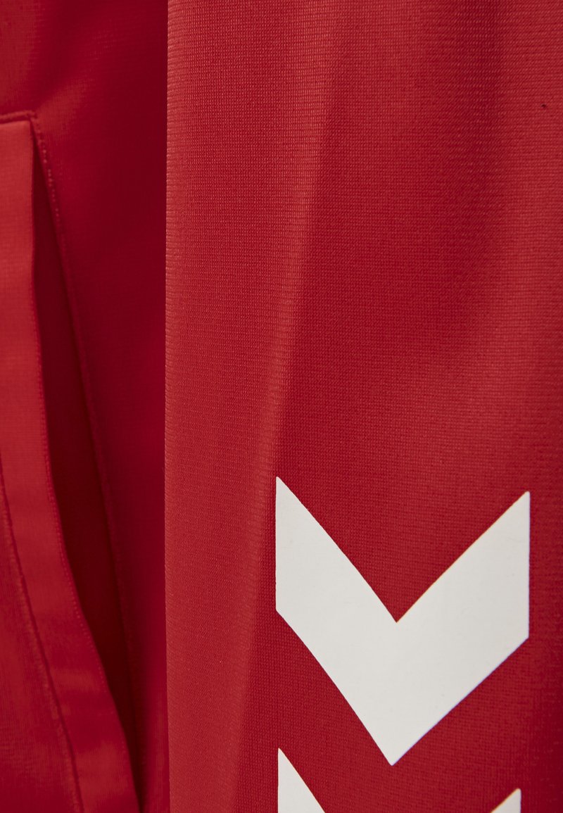 Un tissu rouge avec une finition texturée présente un motif en chevron blanc proéminent. Le design met l'accent sur les lignes verticales et les couleurs vives.