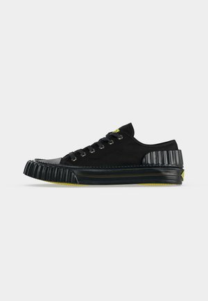 Schwarzer niedriger Sneaker mit gerippter Gummisohle und Ferse, Schnürverschluss und gelben Akzenten an Sohle und Zunge.