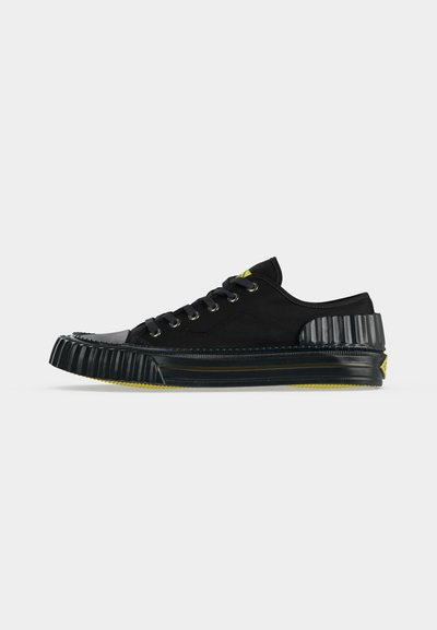 Baskets basses noires avec semelle et talon en caoutchouc nervuré, fermeture à lacets et accents jaunes sur la semelle et la languette.
