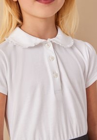 Fehér pamut polo ing fodros gallérral, rövid ujjakkal és három szövetborítású gombbal a nyaknál.