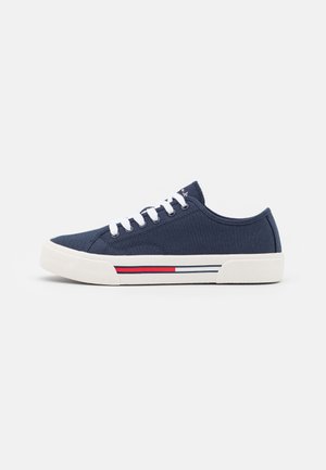 Donkerblauwe lage canvas sneaker met witte veters en zool, met een rood-zwarte streep aan de zijkant.