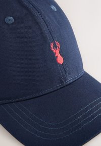 Marinblå basebollkeps med broderad röd hummerdesign. Har texturerat tyg, böjd skärm och kontrasterande sömmar.