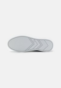 Suela de zapato de goma blanca con un patrón texturizado, que presenta surcos diagonales y un diseño de flecha para mejorar la tracción y el agarre.