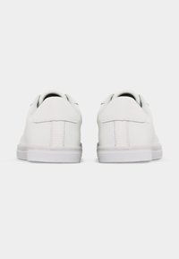 Paire de baskets basses blanches et propres vues de dos sur un fond blanc uni.