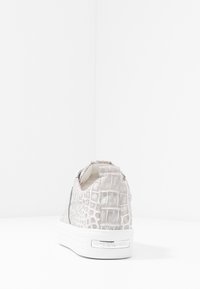 Basket gris avec texture crocodile, semelle en caoutchouc blanche, design sans lacets et talon rembourré pour le confort. Présente un logo sur le côté.