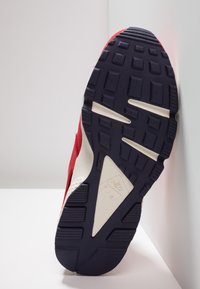 Sula av en röd och vit Nike Air sneaker med svart mönster som vilar mot en vit hörnyta.