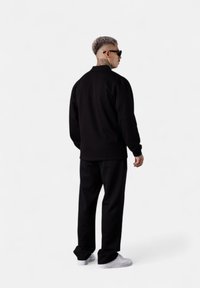 Schwarz sweatshirt mit Rundhalsausschnitt und lockeren Hosen, aus weichem Material mit glatter Textur. Tragen mit weißen Sneakers und Sonnenbrille.